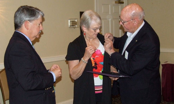 Willis Berry attaches the Paul Harris Fellow pin on his wife’s lapel as Dr. Don Robinson looks on