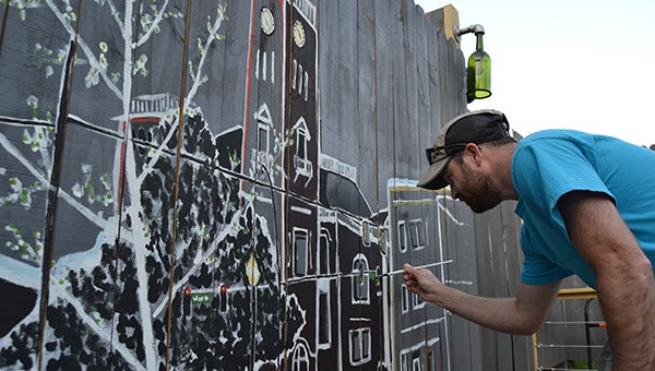 Local artist Ashley Long paints a mural of downtown in The Yard above an herb garden. 